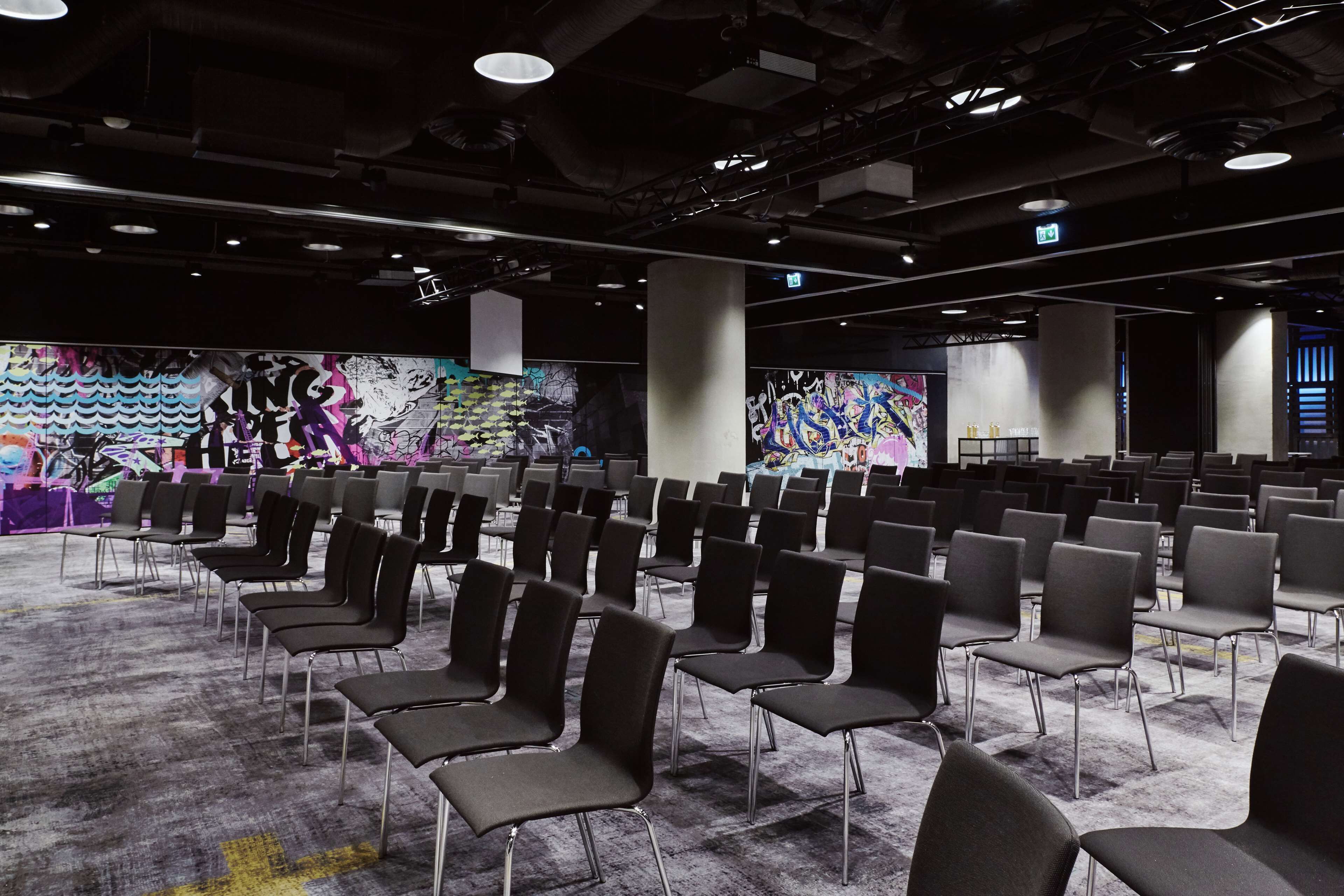 Een congreszaal met rijen stoelen, een vloerbedekking en graffiti op de muren.