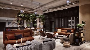 A modern lounge area with sofas, chairs, and a coffee table. There is a staircase in the background, and a large pillar with a plant on top. - Radisson Blu Seaside Hotel, Helsinki (Helsinki)