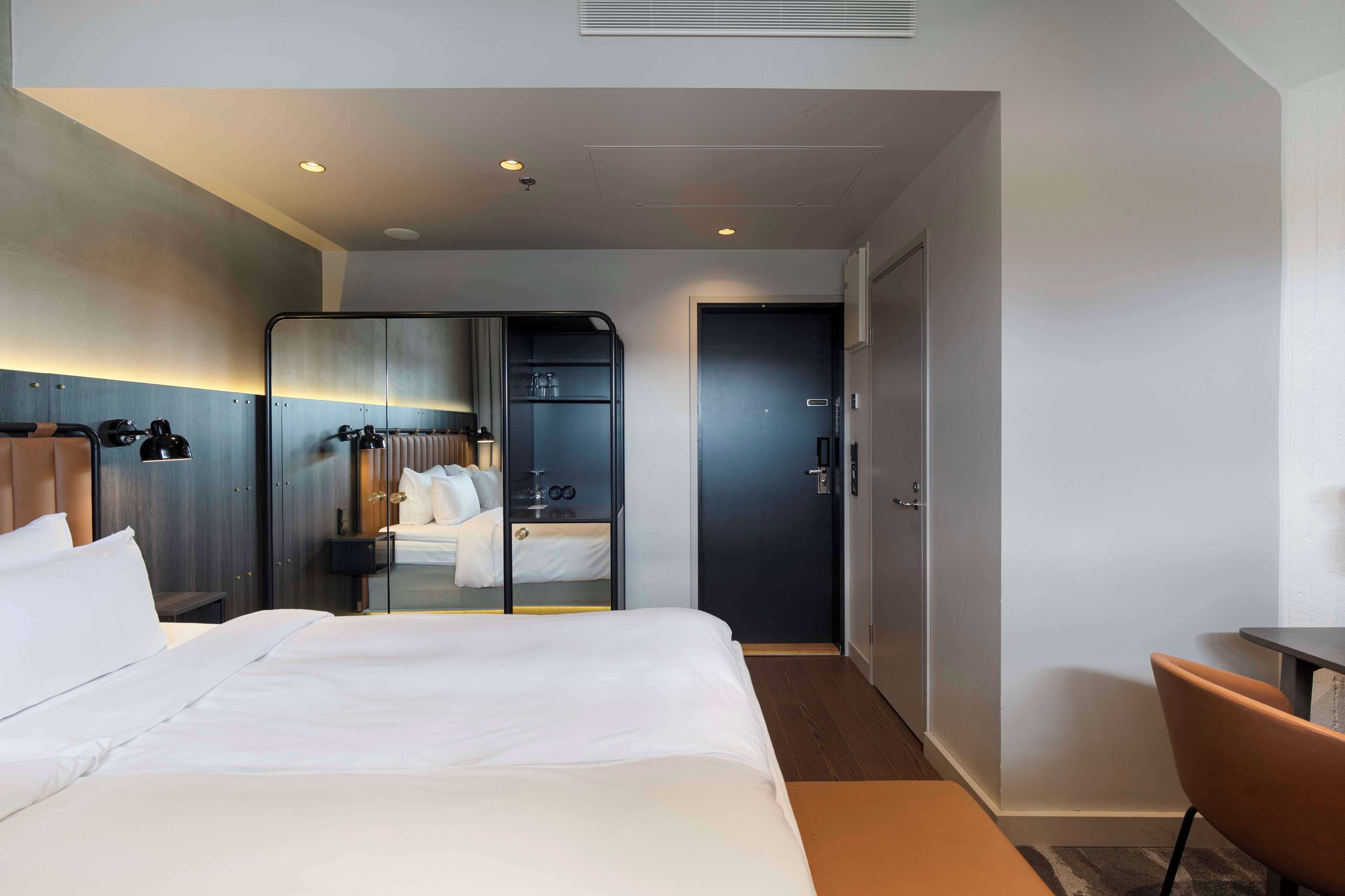 Ett hotellrum med en stor säng, ett skrivbord, en stol, en garderob och en dörr.
