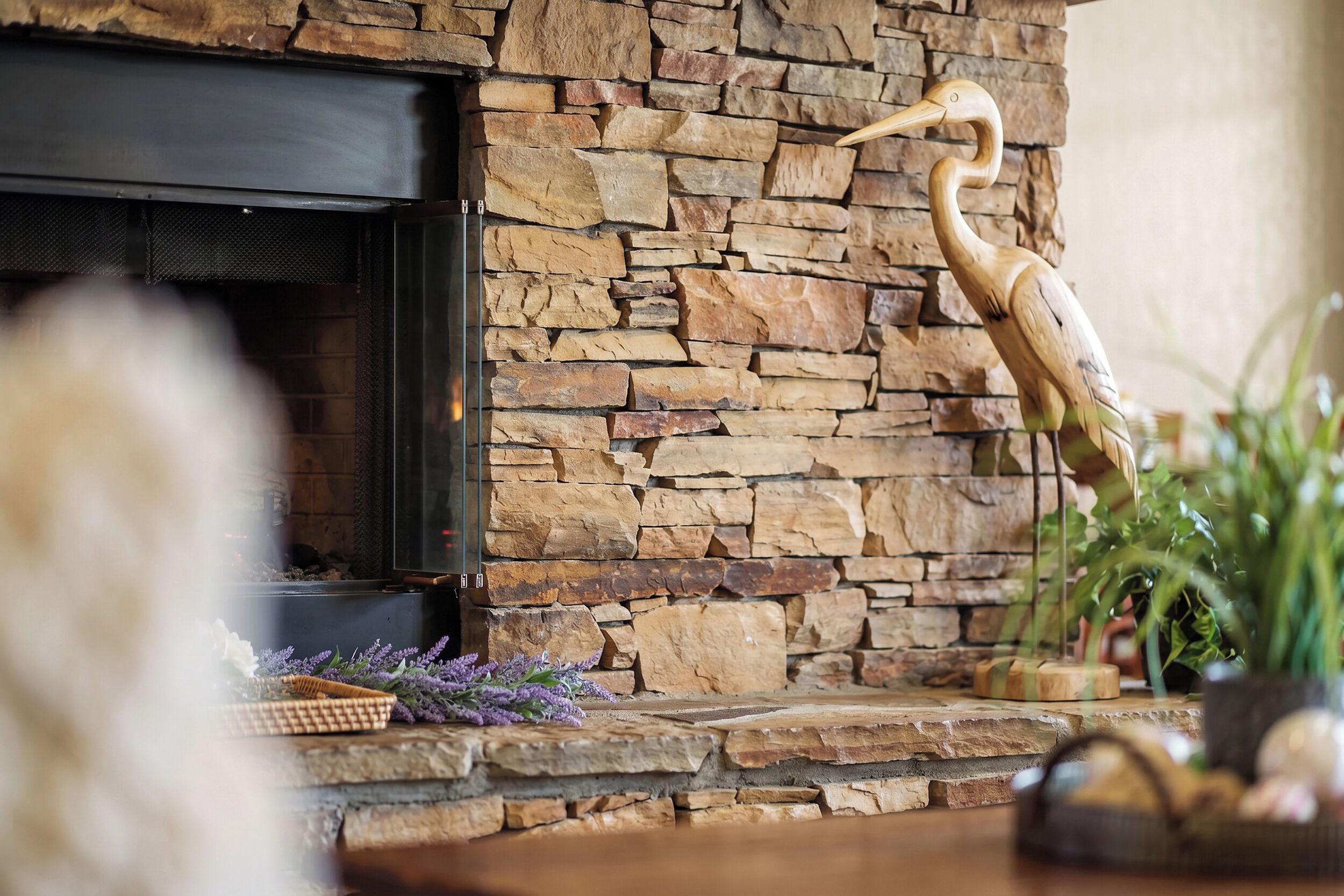 Una chimenea de piedra con una escultura de pájaro de madera, una cesta con flores y una planta en maceta.