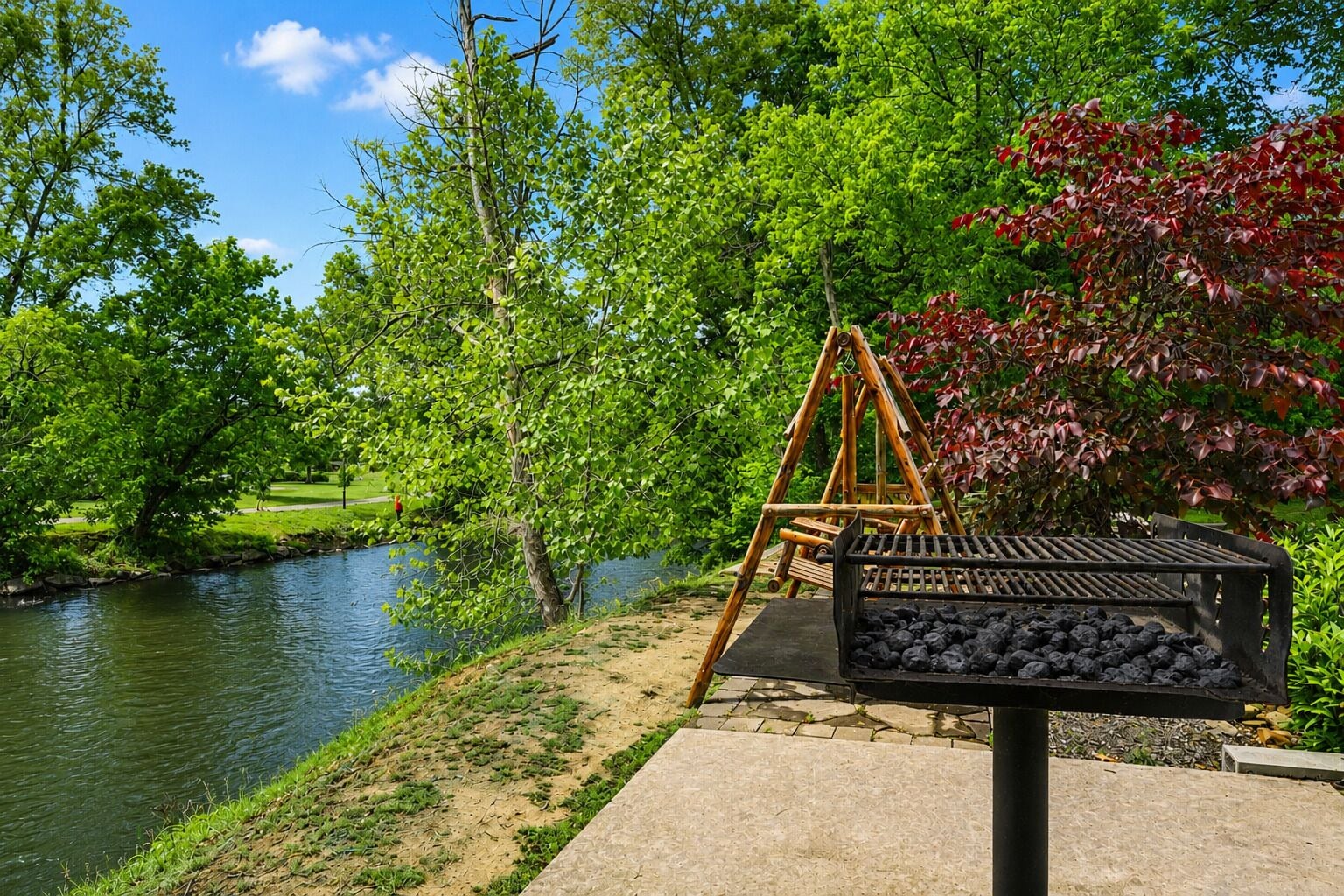 A riverside park with a swing set and a charcoal grill.