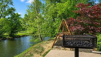 A riverside park with a swing set and a charcoal grill.