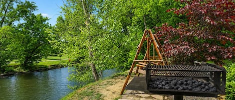 A riverside park with a swing set and a charcoal grill.