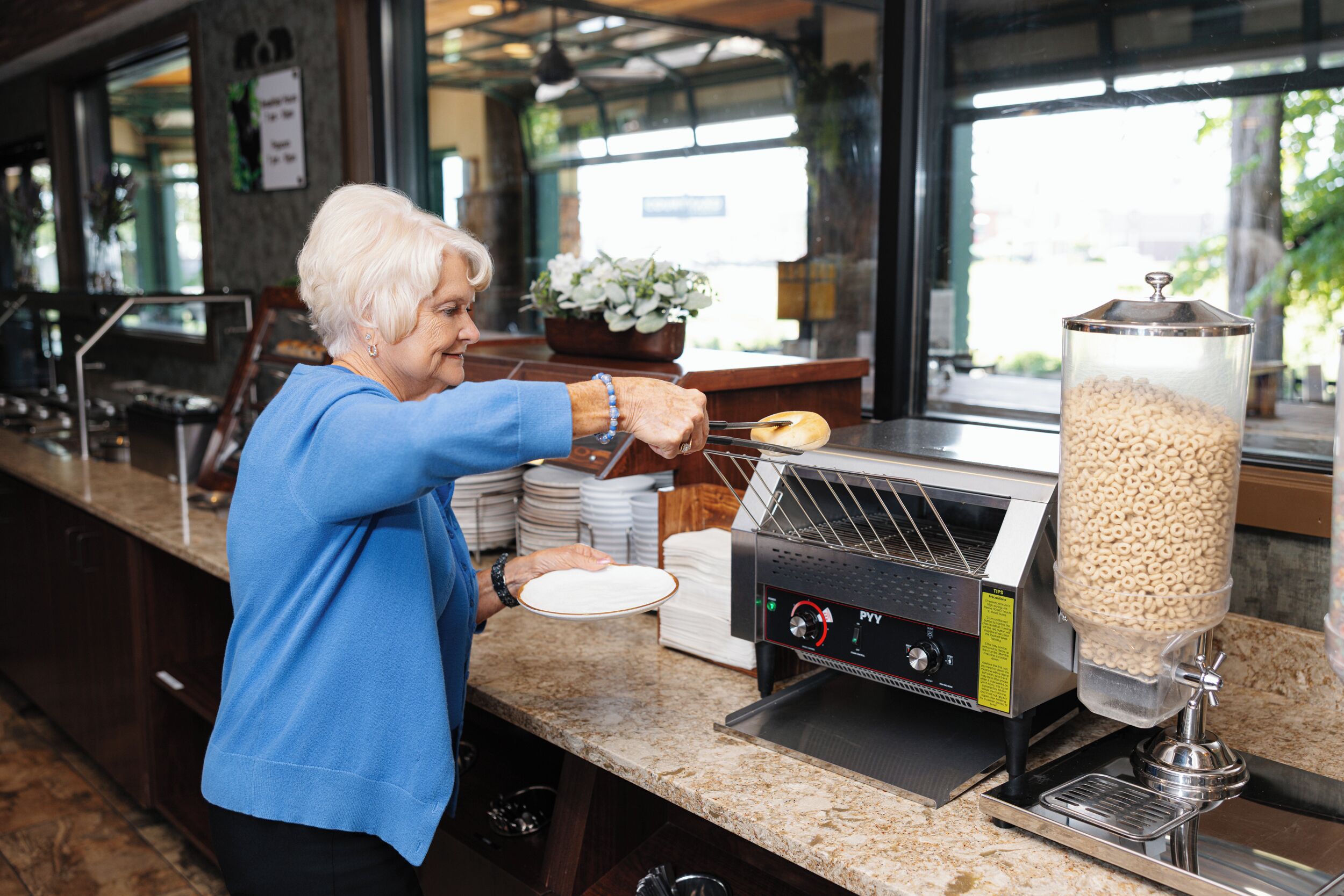 A person serving cereal from a dispenser at a counter with a window view.