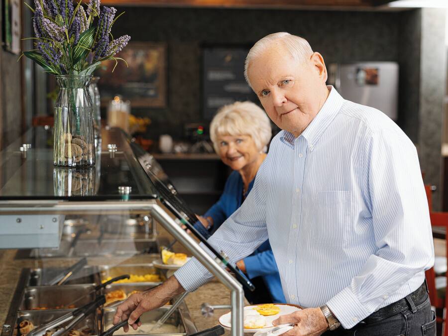 A buffet area with multiple food stations, a vase with flowers, and a person serving food.