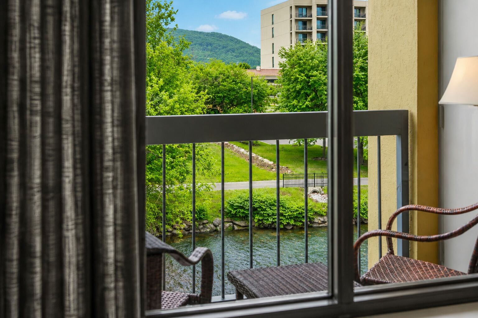 A balcony with a view of a landscaped garden, a small water feature, and a building in the background.