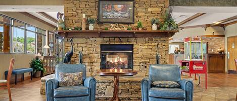 A stone fireplace with a framed picture above, two blue leather chairs with cushions, a small table, and a popcorn cart.
