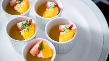 Quatro pequenas tigelas brancas com uma sobremesa amarela, decorada com morangos e salsa, sobre um prato branco.
