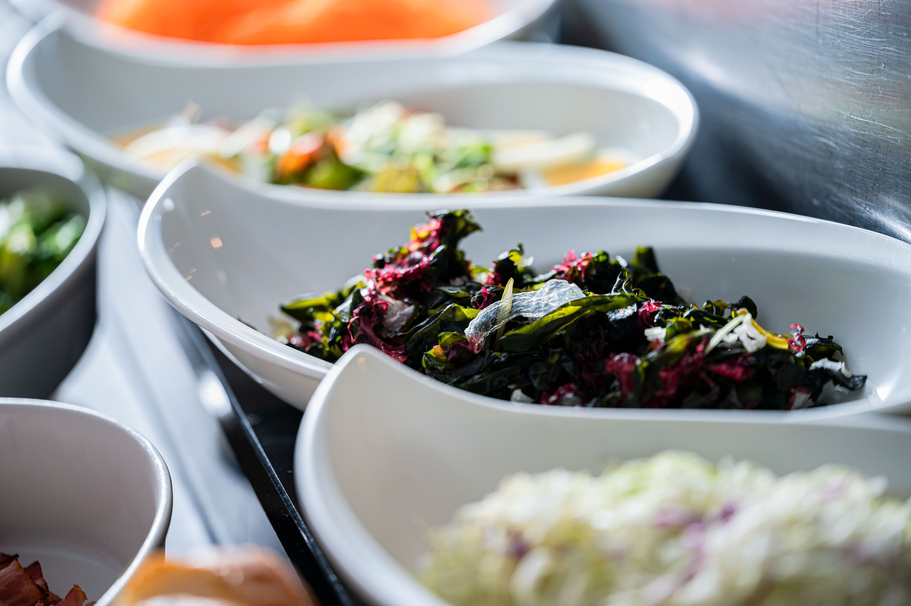 A variety of dishes in white bowls, including greens and a coleslaw.