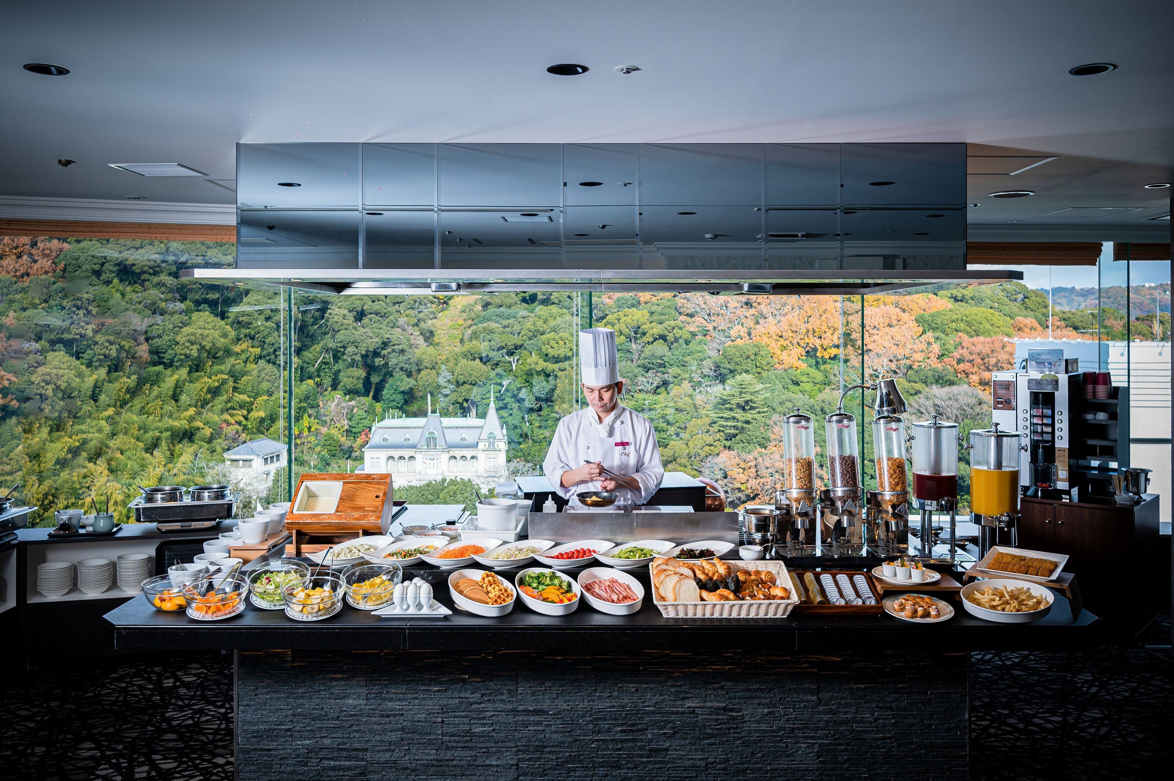 A chef preparing food in a modern kitchen with a scenic view of a forested area.