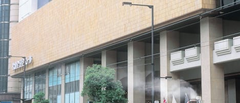 A steam train with a conductor, passing by a modern building with large windows and a flat roof.
