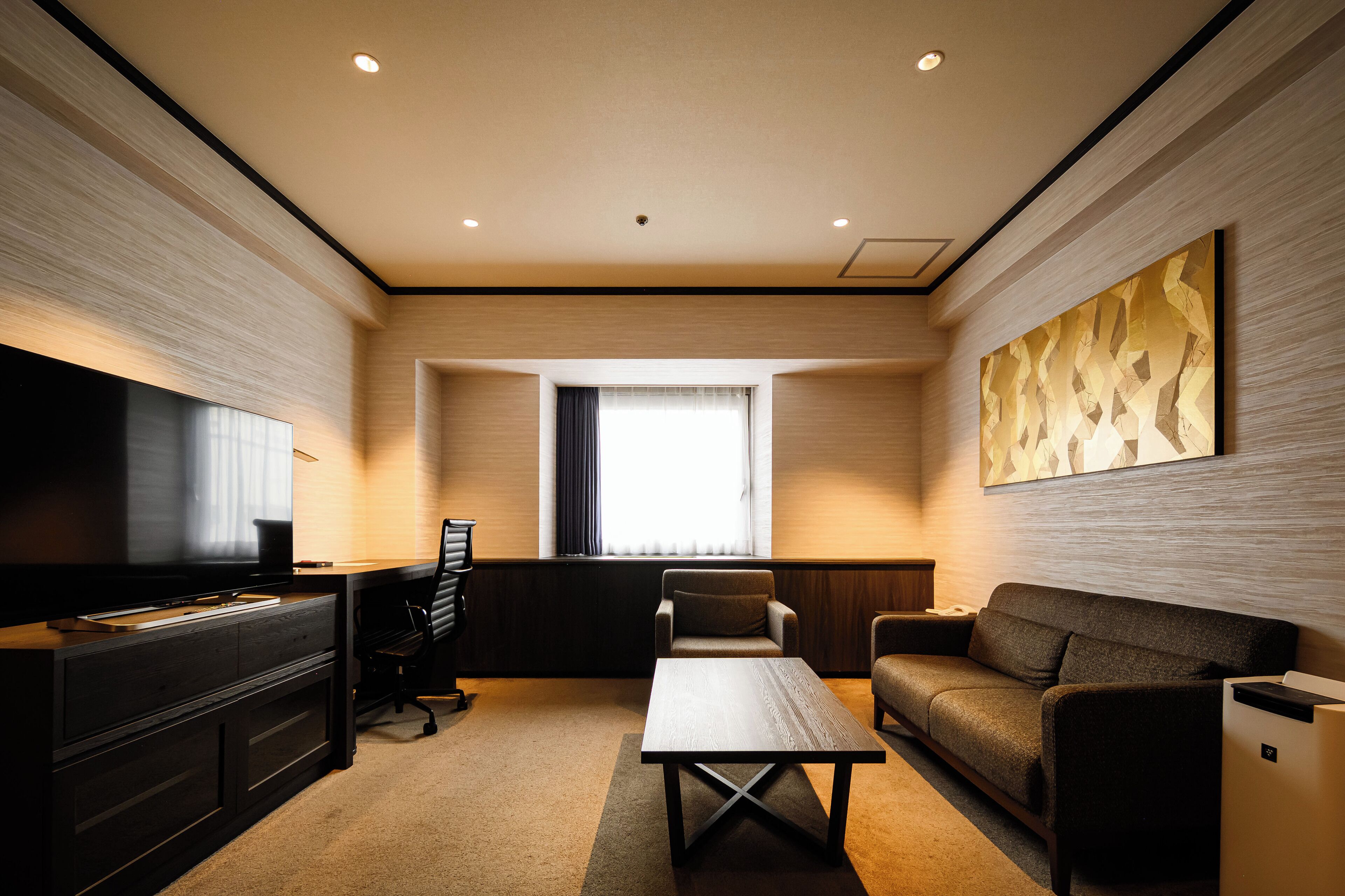 Ein modernes Hotelzimmer mit Flachbildfernseher, einer Couch, einem Couchtisch und einem großen abstrakten Gemälde an der Wand.