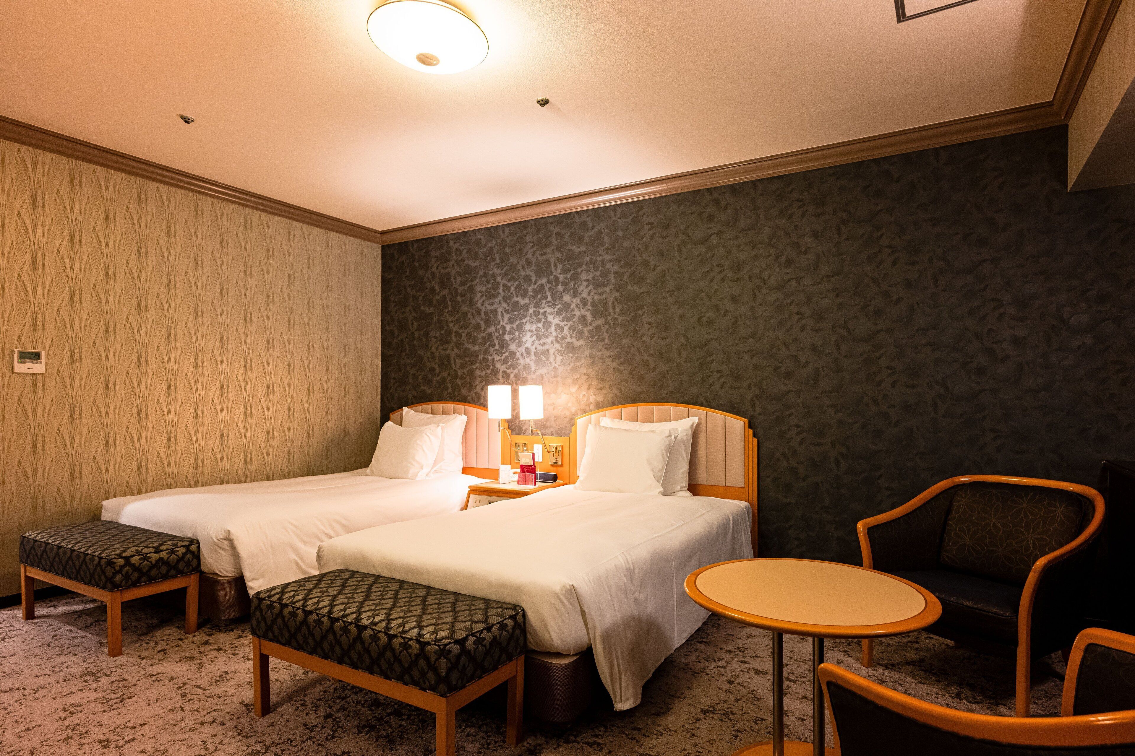 Habitación de hotel con dos camas, una mesita, una silla y un banco.