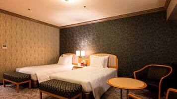 A hotel room with two beds, a small table, a chair, and a bench.
