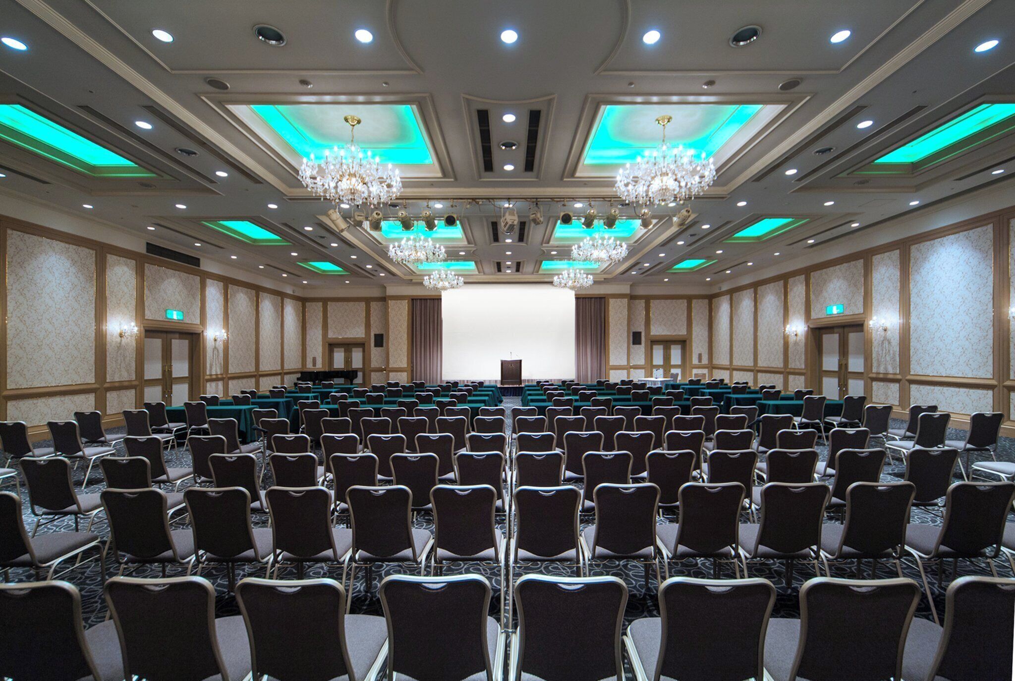 A large conference room with rows of chairs, a stage with a podium, and chandeliers.