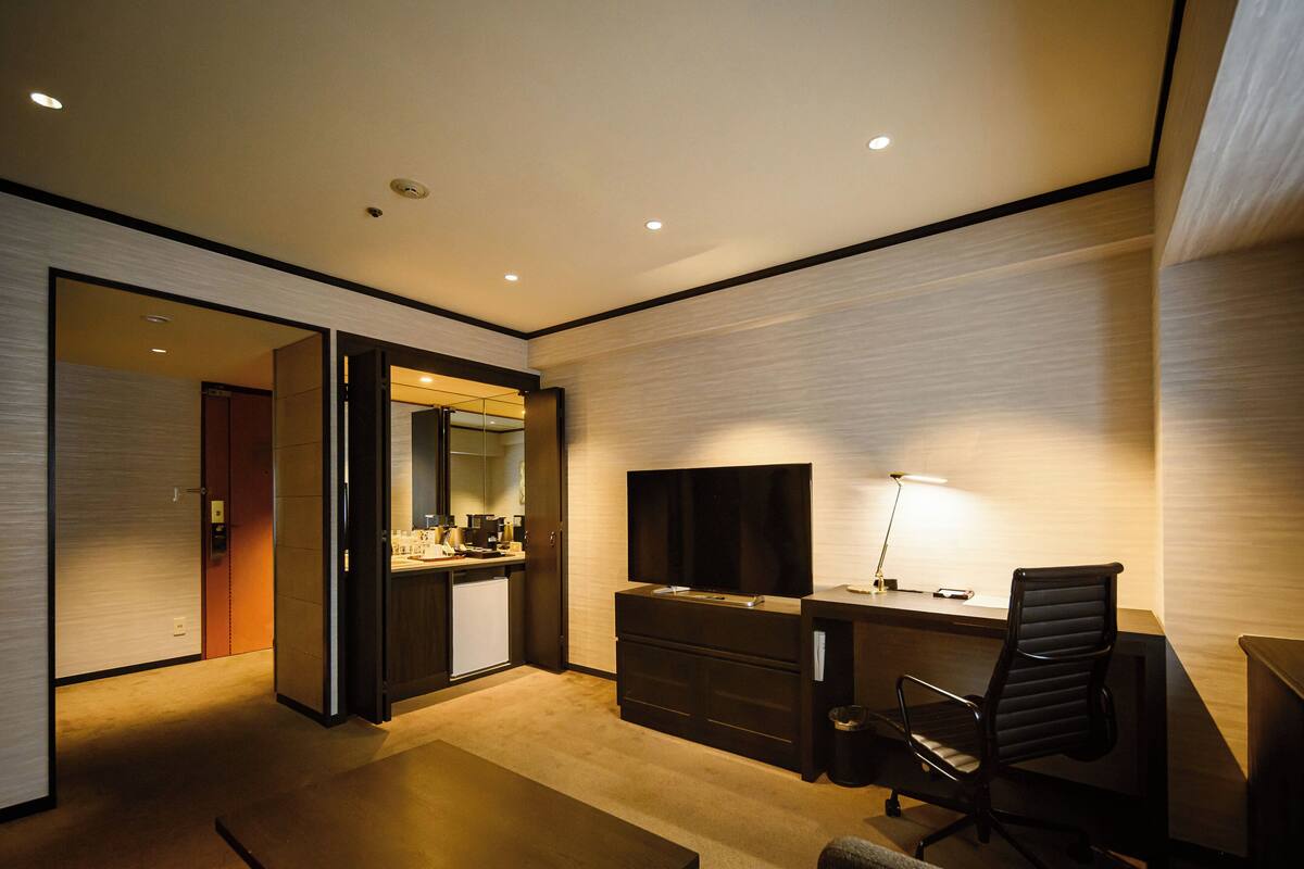 Una habitación de hotel moderna con escritorio, silla, televisión y una pequeña kitchenette.