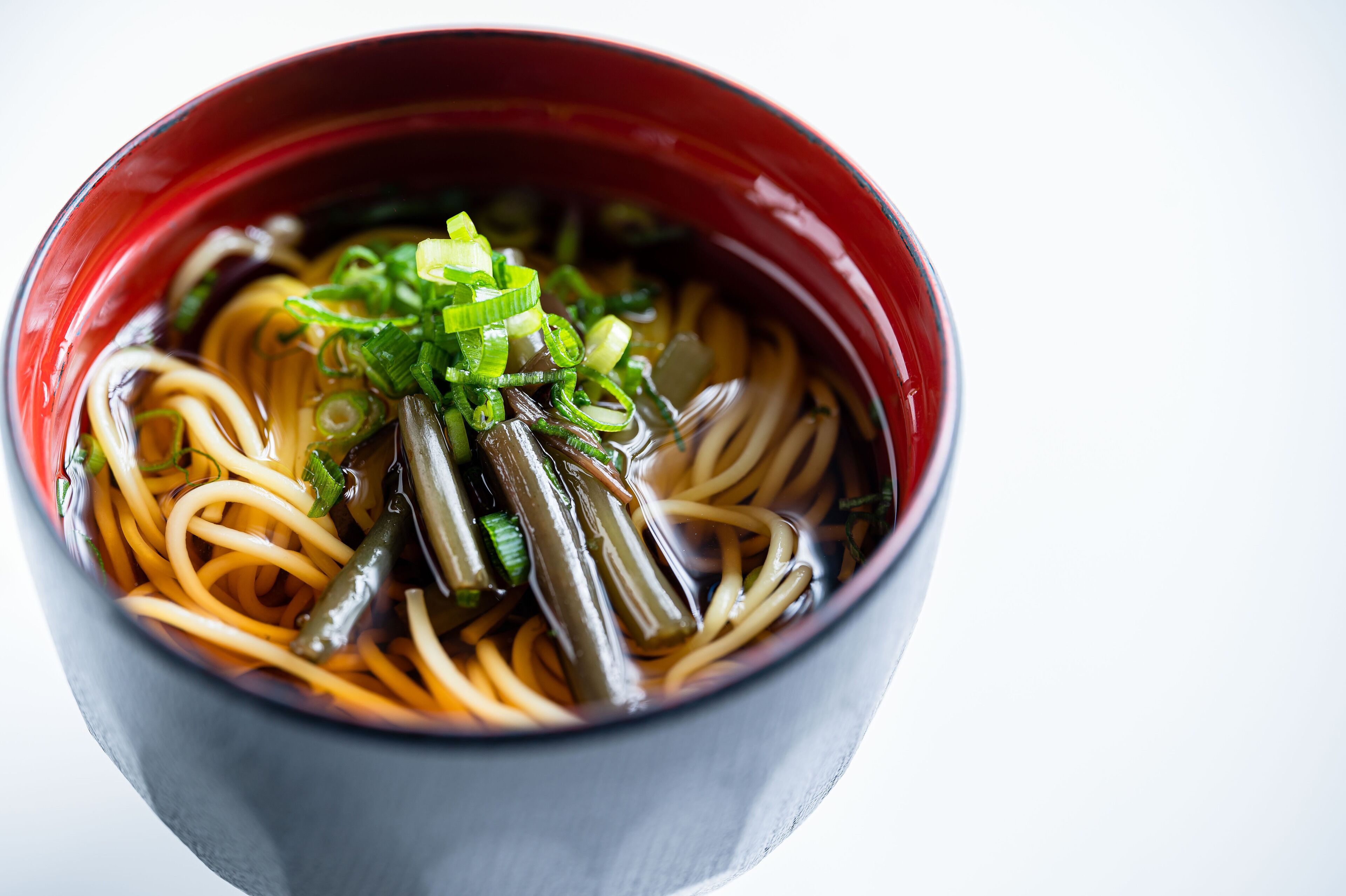 A bowl of ramen with noodles, green onions, and green vegetables.