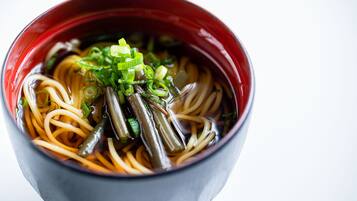 A bowl of ramen with noodles, green onions, and green vegetables.