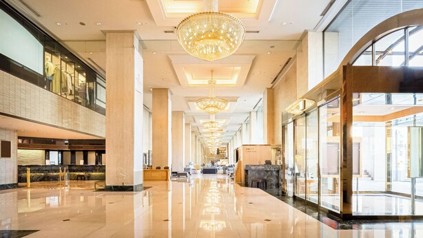 Eine großzügige Lobby mit hoher Decke, mehreren Kronleuchtern und einer Glasfassade an einer Seite.