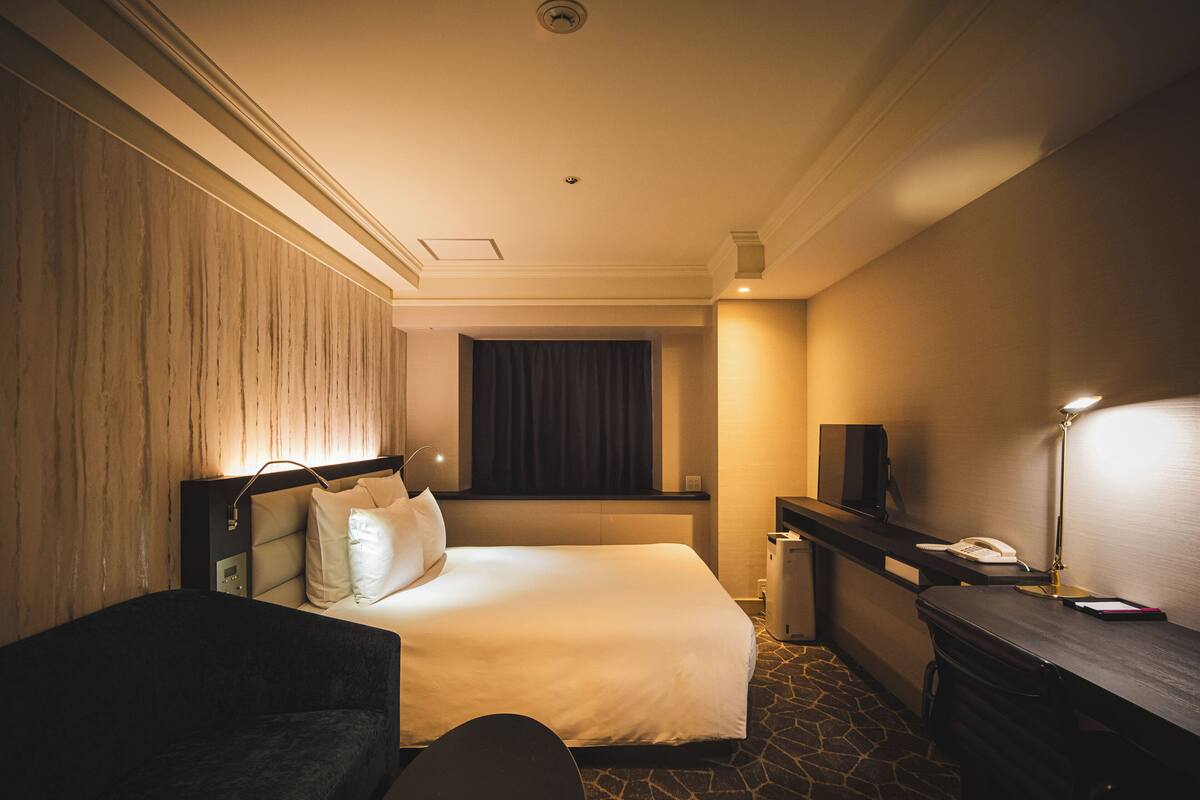 Una habitación de hotel con cama, mesita de noche, lámpara y escritorio con teléfono.