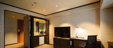 Una habitación de hotel moderna con escritorio, silla, televisión y una pequeña kitchenette.