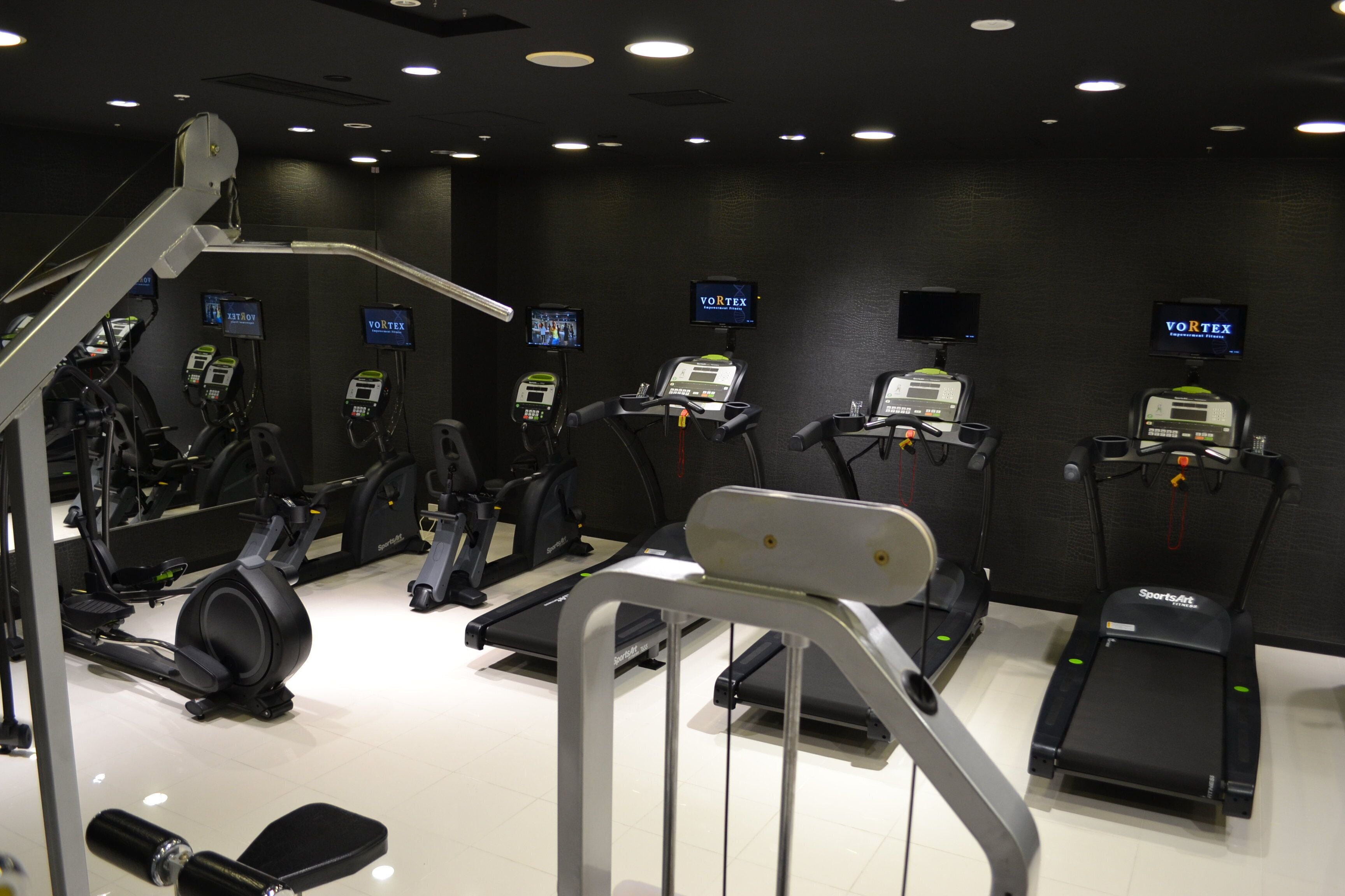 A gym with multiple exercise machines, including treadmills and stationary bikes, arranged in rows.