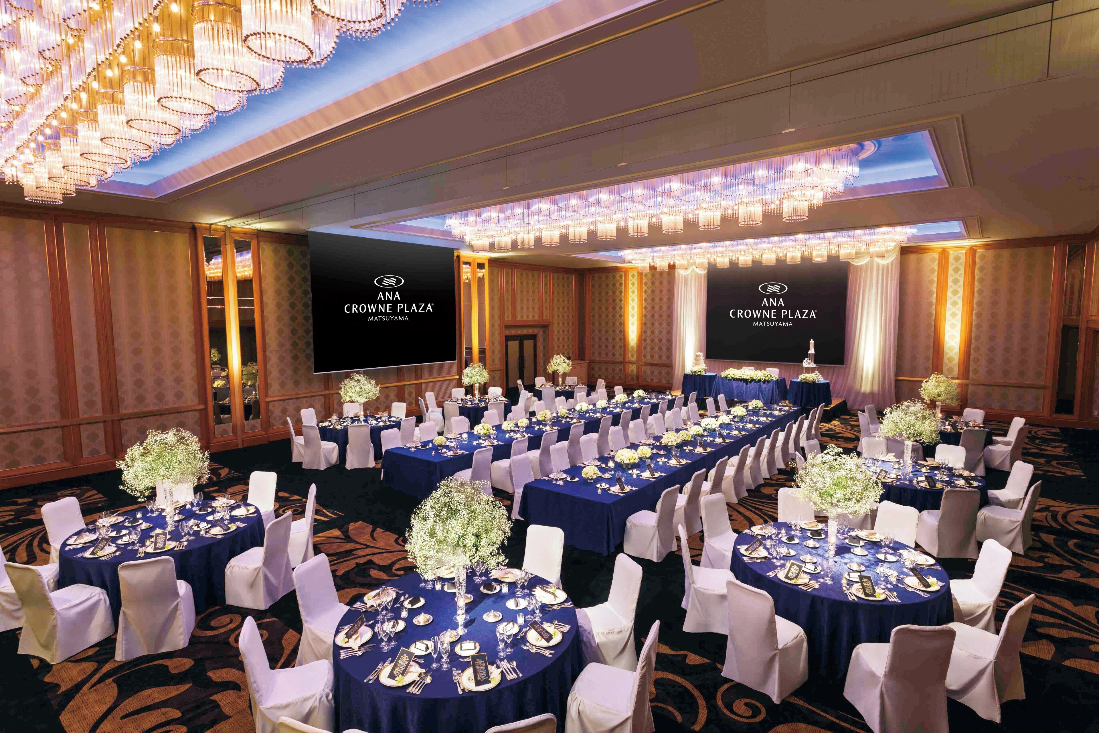 A conference room at ANA Crowne Plaza Matsuyama with round tables, white chairs, and chandeliers.