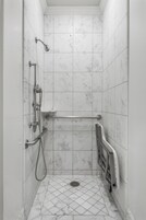 Box de chuveiro estreito com revestimento em azulejos, chuveiro manual e barra de apoio.