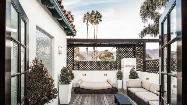 A patio with a sofa and a small table, surrounded by potted plants and a wooden deck. - Montecito Inn (Santa Barbara)