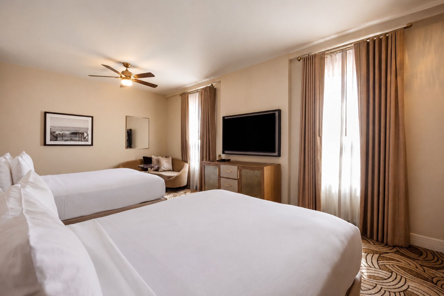 A hotel room with two beds, a ceiling fan, a flat-screen TV, a desk, and a chair.