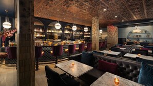 A bar area with a high ceiling, bar stools, and a seating area with tables and chairs. - Montecito Inn (Santa Barbara)