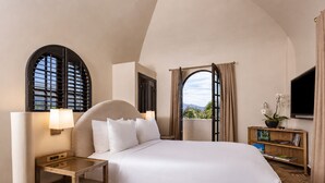 A hotel room with a large bed, a bedside table, a TV, and a bookshelf. - Montecito Inn (Santa Barbara)