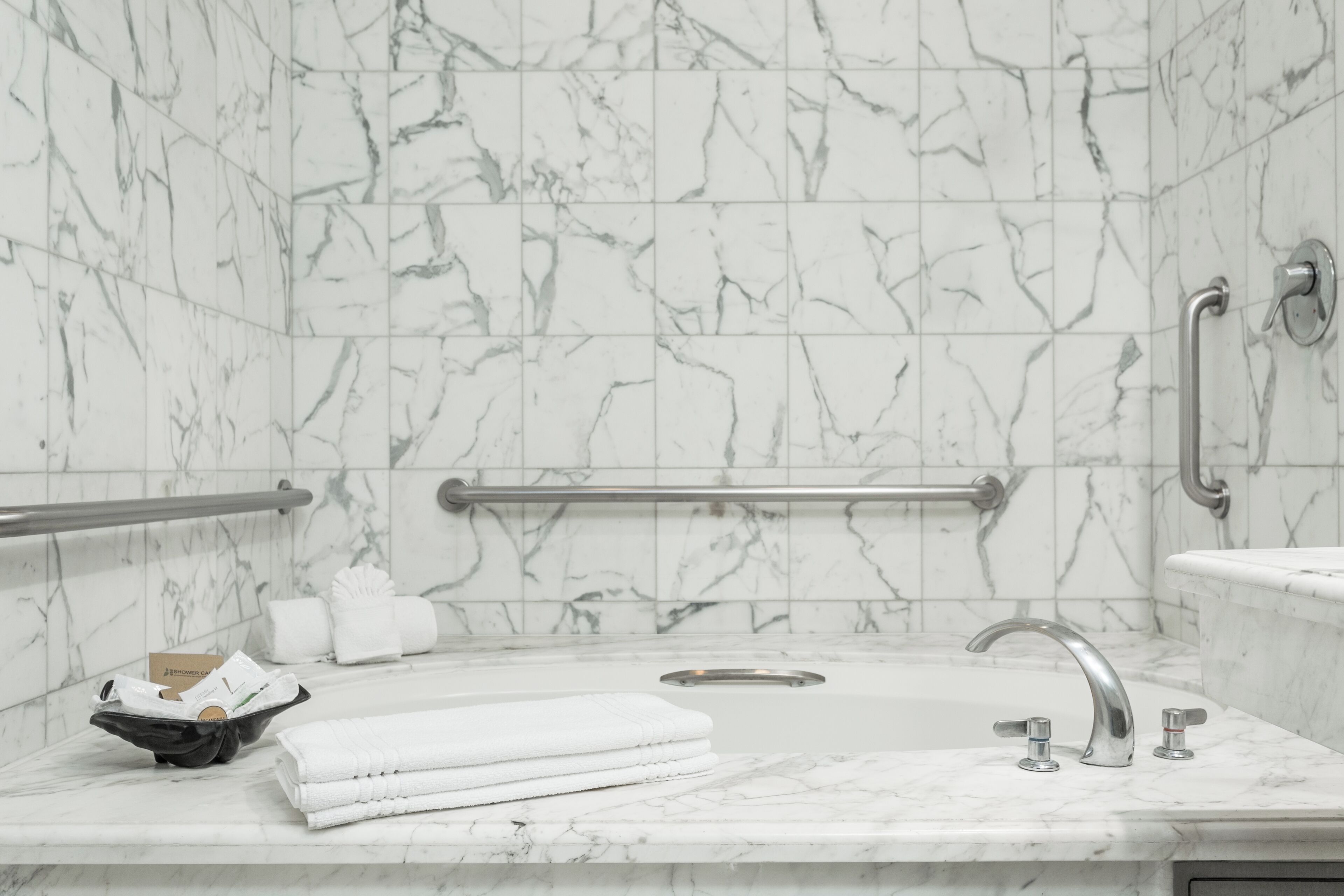 A bathroom with marble walls, a sink with a single faucet, a handrail, and a towel rack.