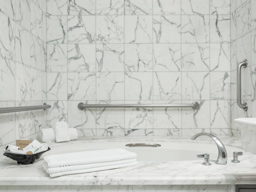 A bathroom with marble walls, a sink with a single faucet, a handrail, and a towel rack.