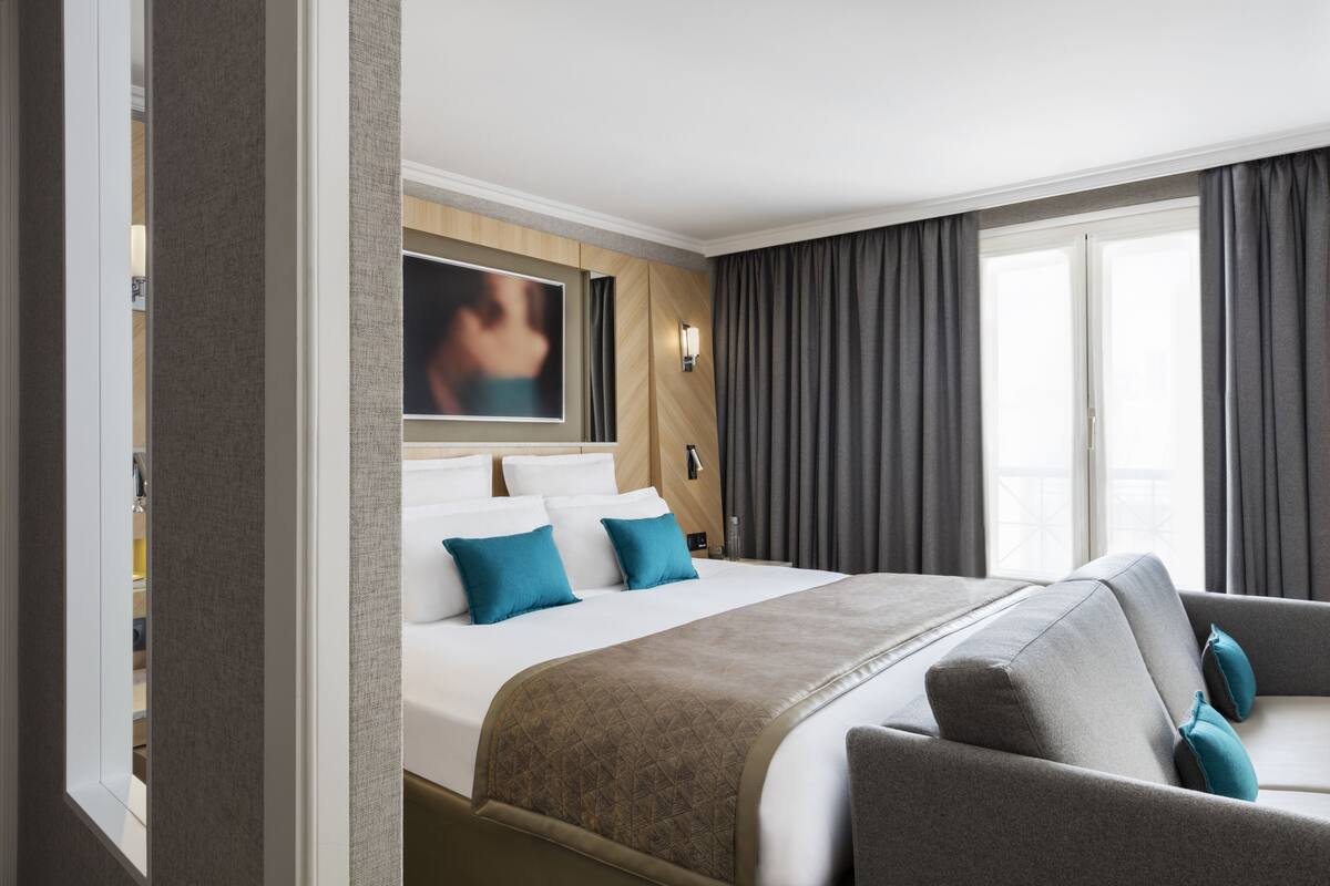 A hotel room with a large bed, a sofa, a TV, and a window with curtains.