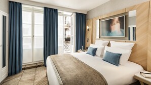 A hotel room with a large bed, a TV mounted on the wall, and a balcony with blue curtains. - Hotel Louvre Saint Honoré (Paris)