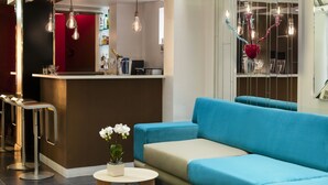 A modern interior with a blue sofa, a bar area, and hanging light fixtures. - Hotel Louvre Saint Honoré (Paris)