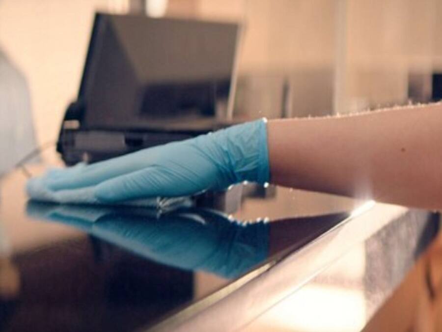 A person wearing a blue glove cleaning a shiny black surface, likely a table or counter.
