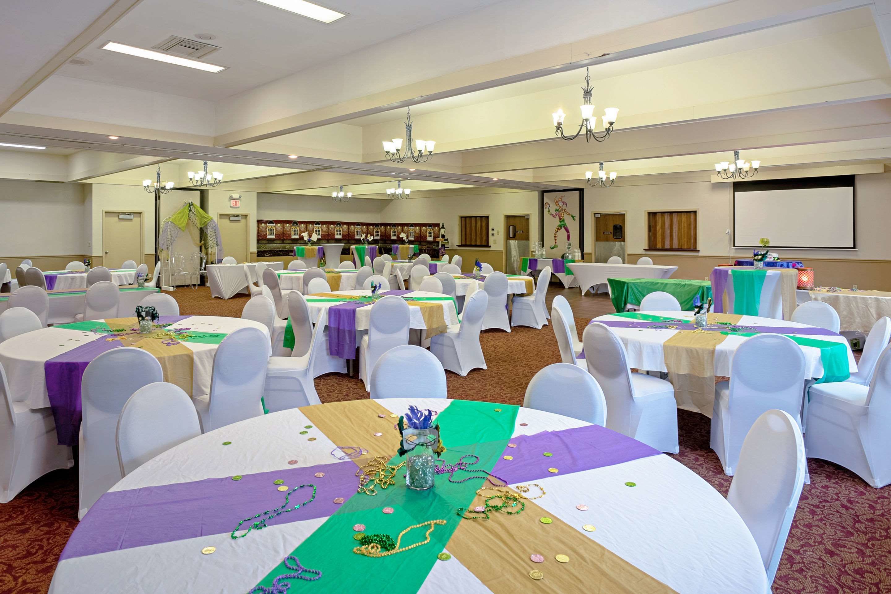 A banquet hall with round tables covered in white tablecloths and green centerpieces, white chairs, and chandeliers.