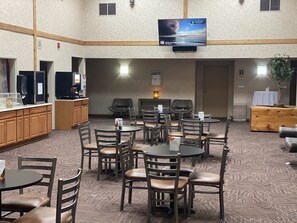 A hotel lobby with multiple seating areas, a television mounted on the wall, and a reception desk.
