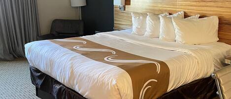A hotel room with a large bed, a headboard, a bedside table, a lamp, and a curtain.