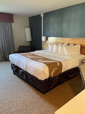 Habitación de hotel con una cama grande, cabecero, mesita de noche, lámpara y cortina.
