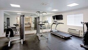 Ein Fitnessstudio mit Laufband, Kraftgeräten und einer Spiegelwand.