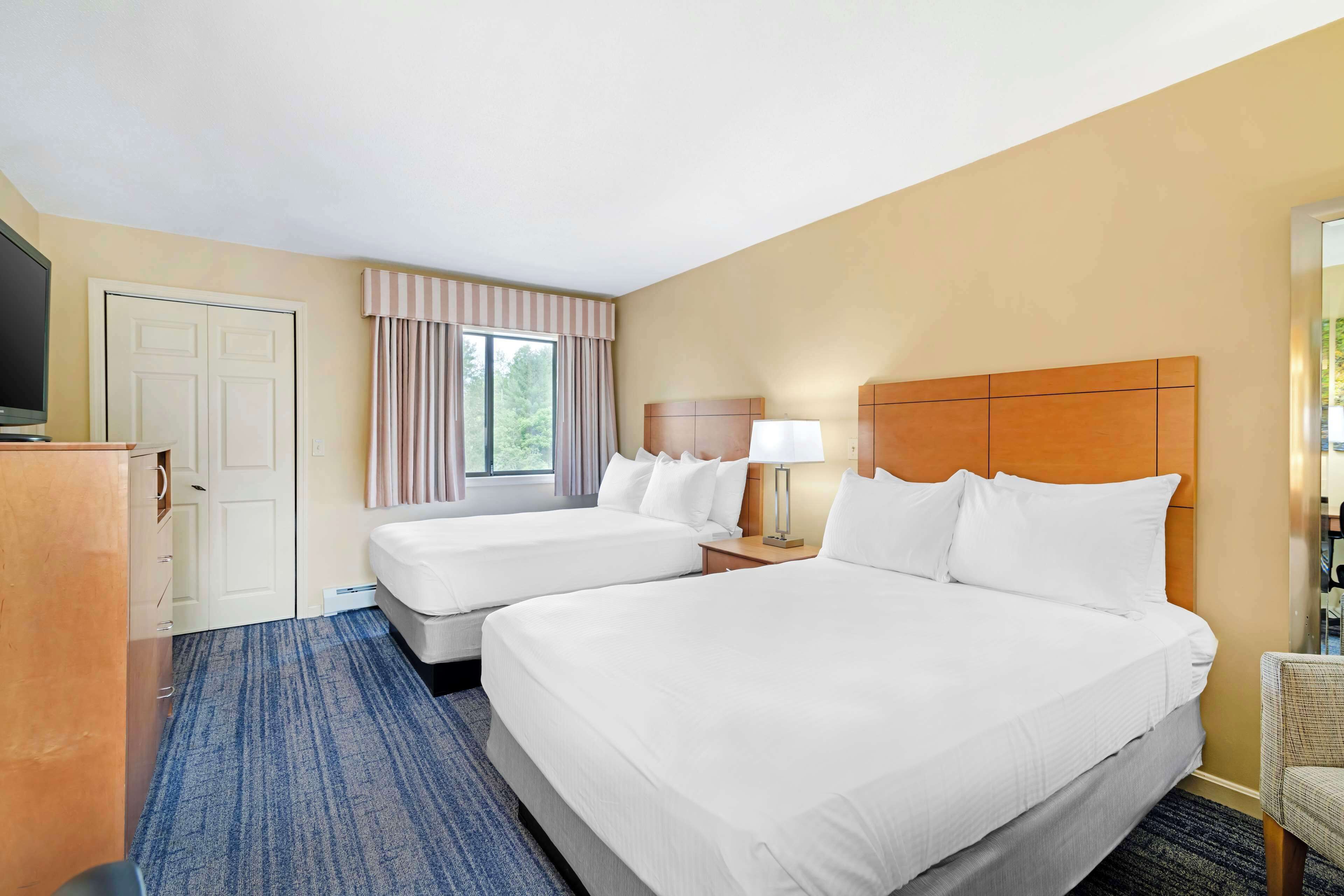A hotel room with two beds, a desk, a TV, and a window with curtains.