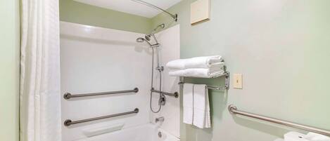 Een badkamer met een bad, een douche en een toilet. Er zijn handgrepen voor toegankelijkheid, een handdoekhouder en een lichtschakelaar aan de muur.
