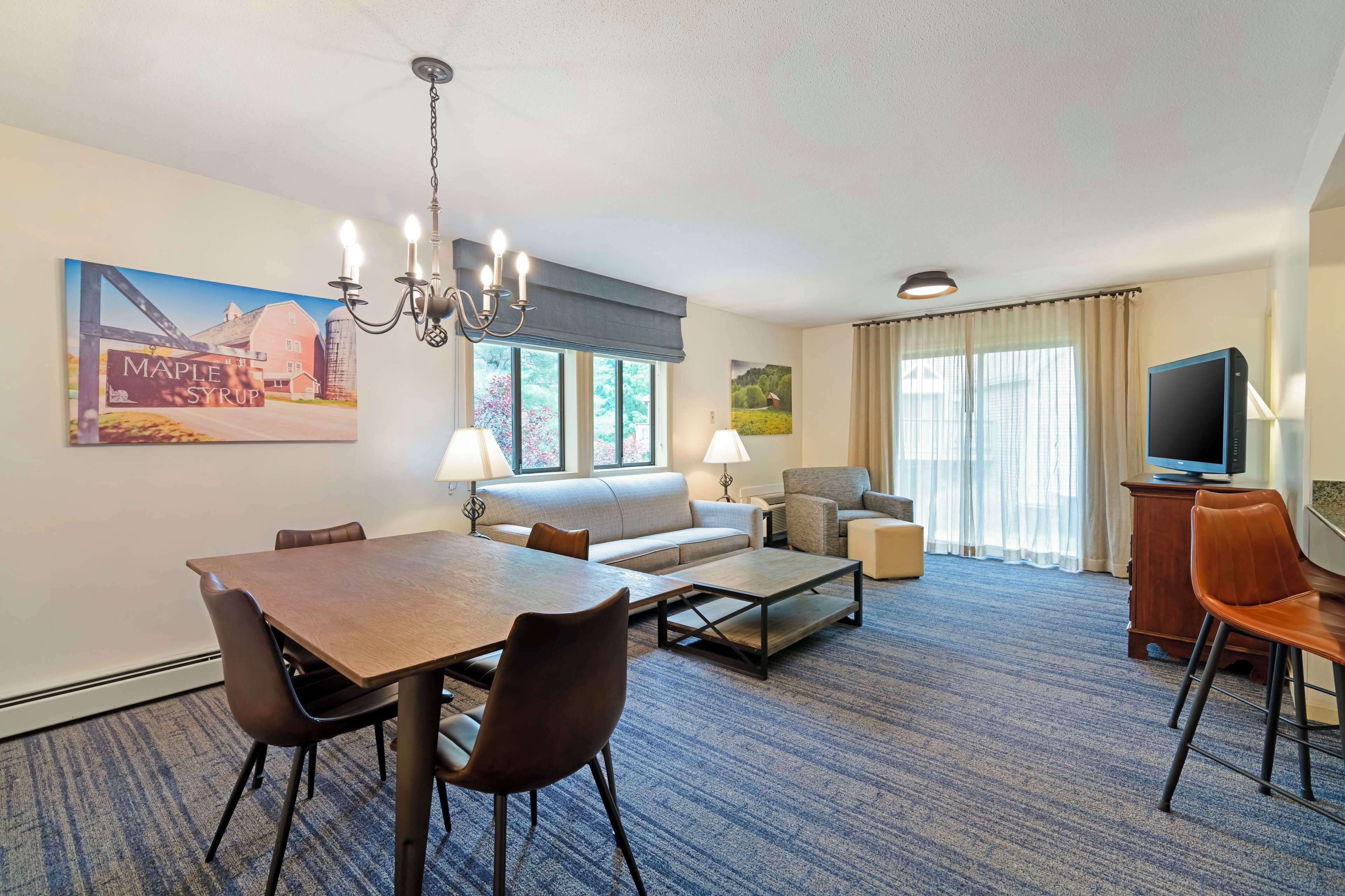 Habitación de hotel con una mesa de comedor, sofá, sillones, televisor y obras de arte en las paredes.