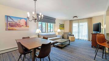 Une chambre d’hôtel équipée d’une table à manger, d’un canapé, de fauteuils, d’un téléviseur et d’œuvres d’art accrochées aux murs.
