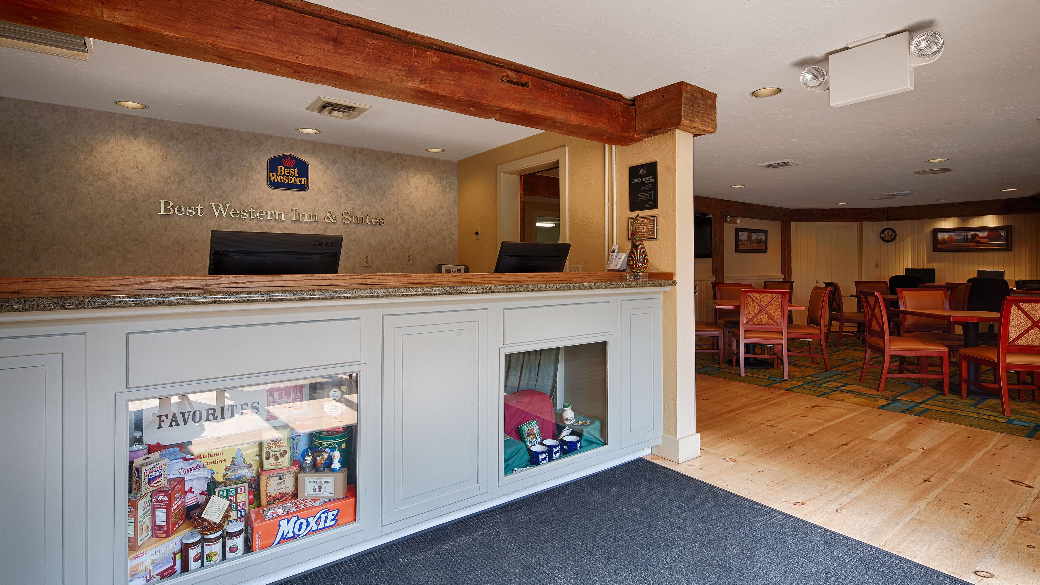 A reception area with a wooden ceiling, a counter with a computer, and a view into a room with a dining area.