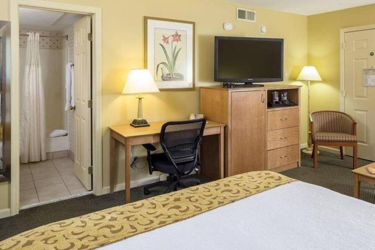 A hotel room with a bed, desk, chair, television, and a bathroom visible through an open door.