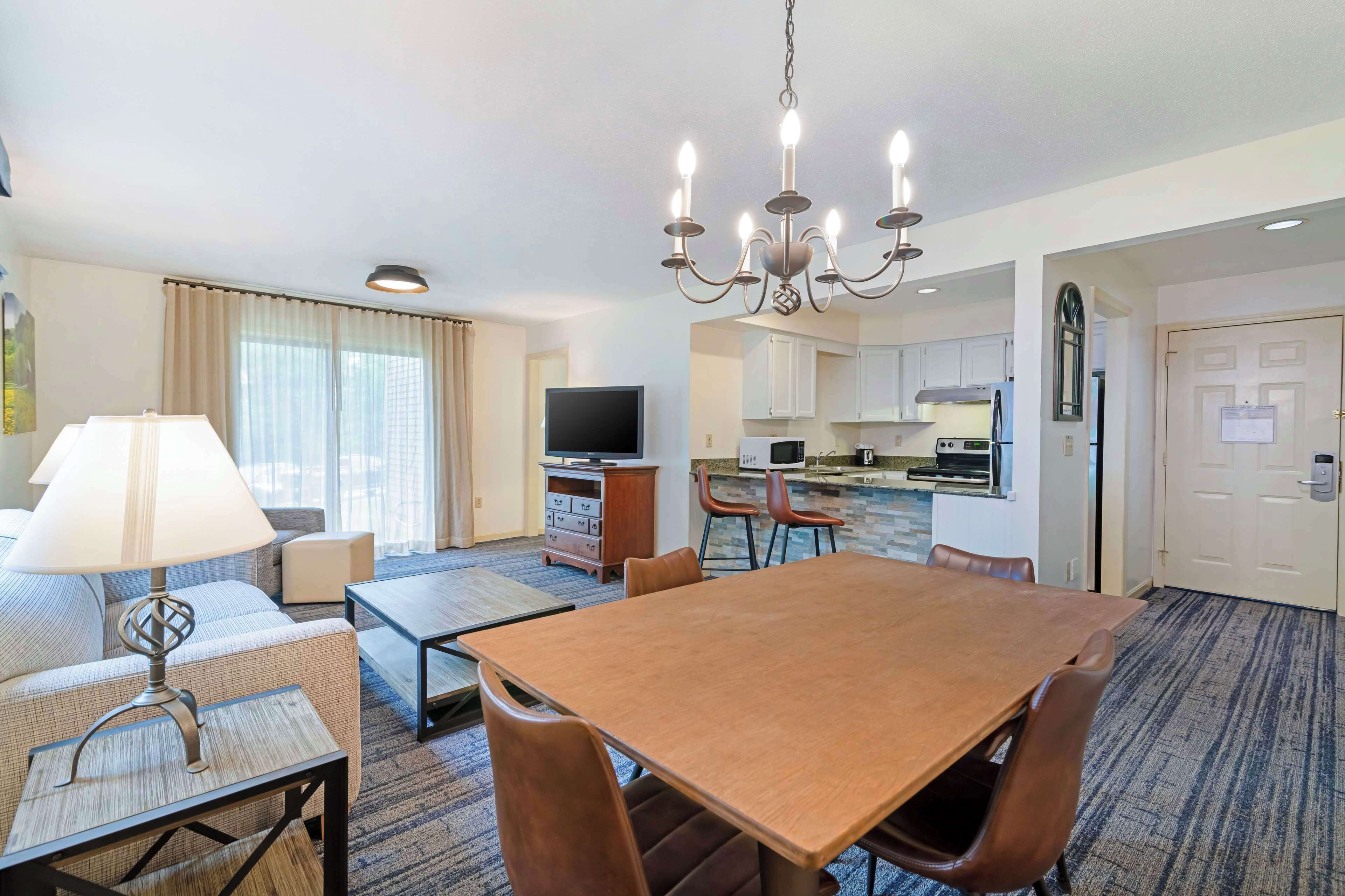A hotel room with a dining area, kitchenette, and a TV.